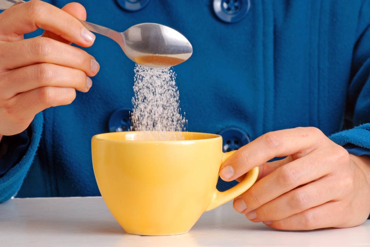 man pouring spoonful of sugar into mug